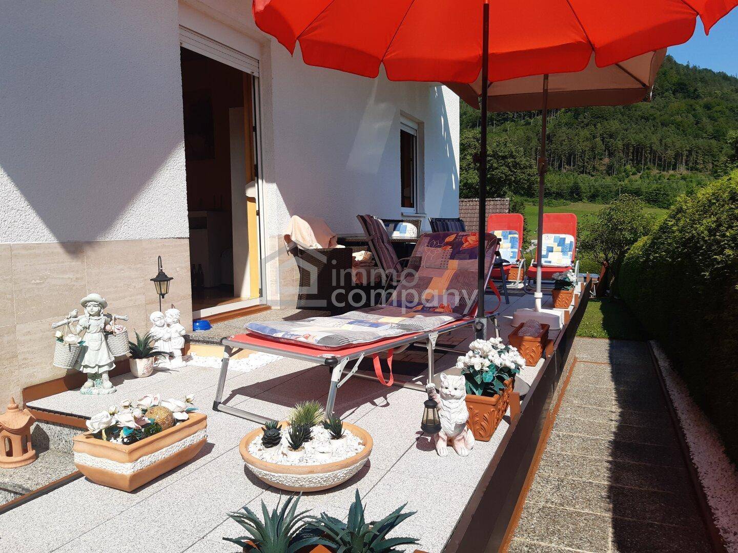 Sonnige Terrasse mit bequemen Liegestühlen, Sonnenschirm und Blick ins Grüne.