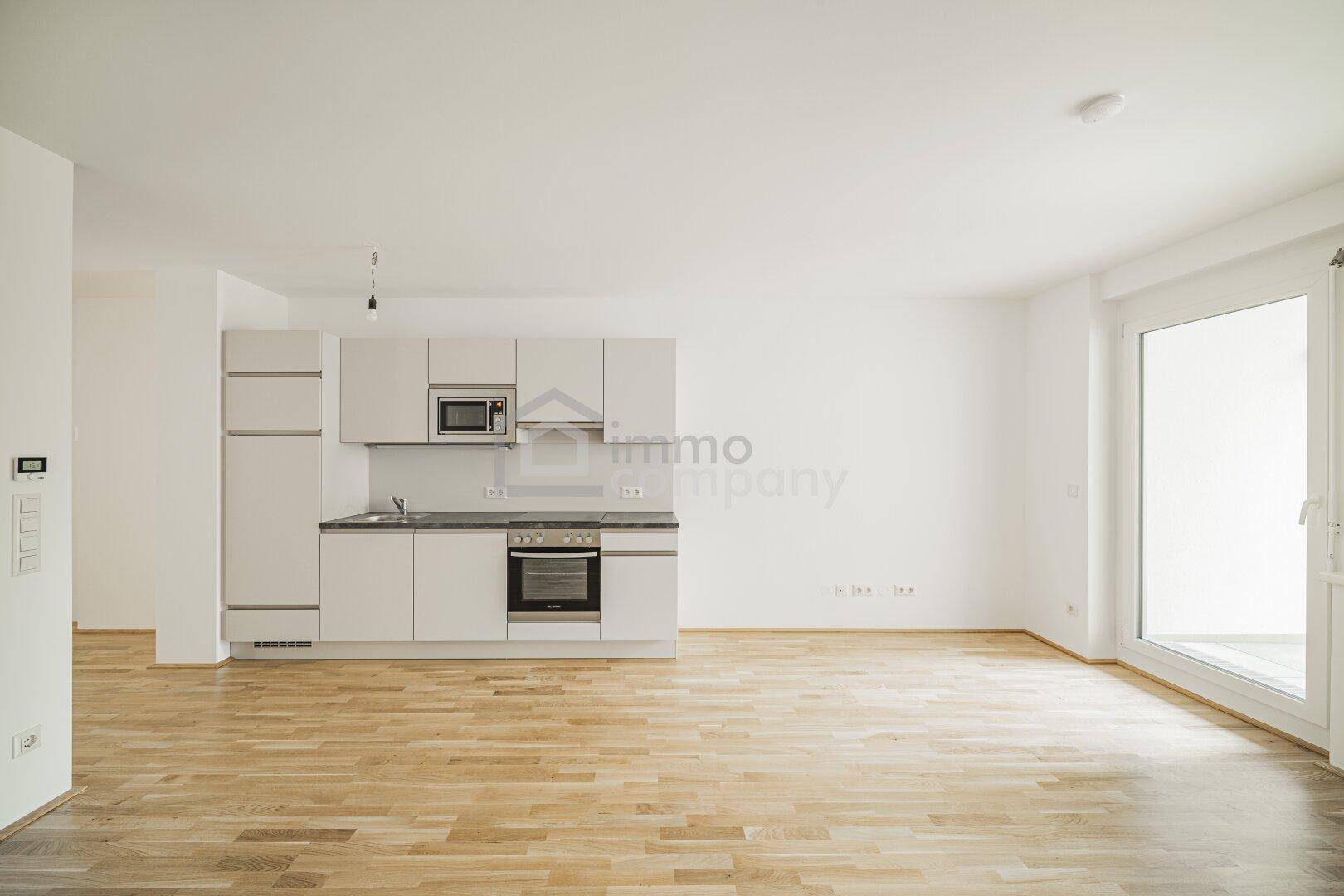 Lichtdurchfluteter Wohnbereich mit Küchenzeile, Parkettboden und Zugang zum Balkon.