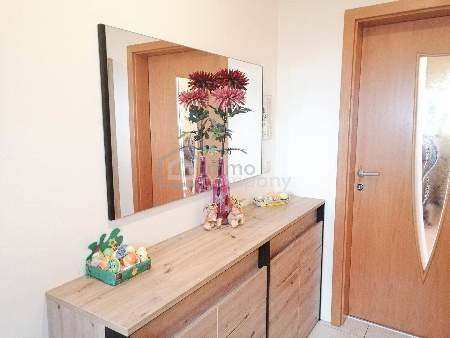 Heller Eingangsbereich mit Holzkommode, großem Spiegel und frühlingshafter Dekoration.