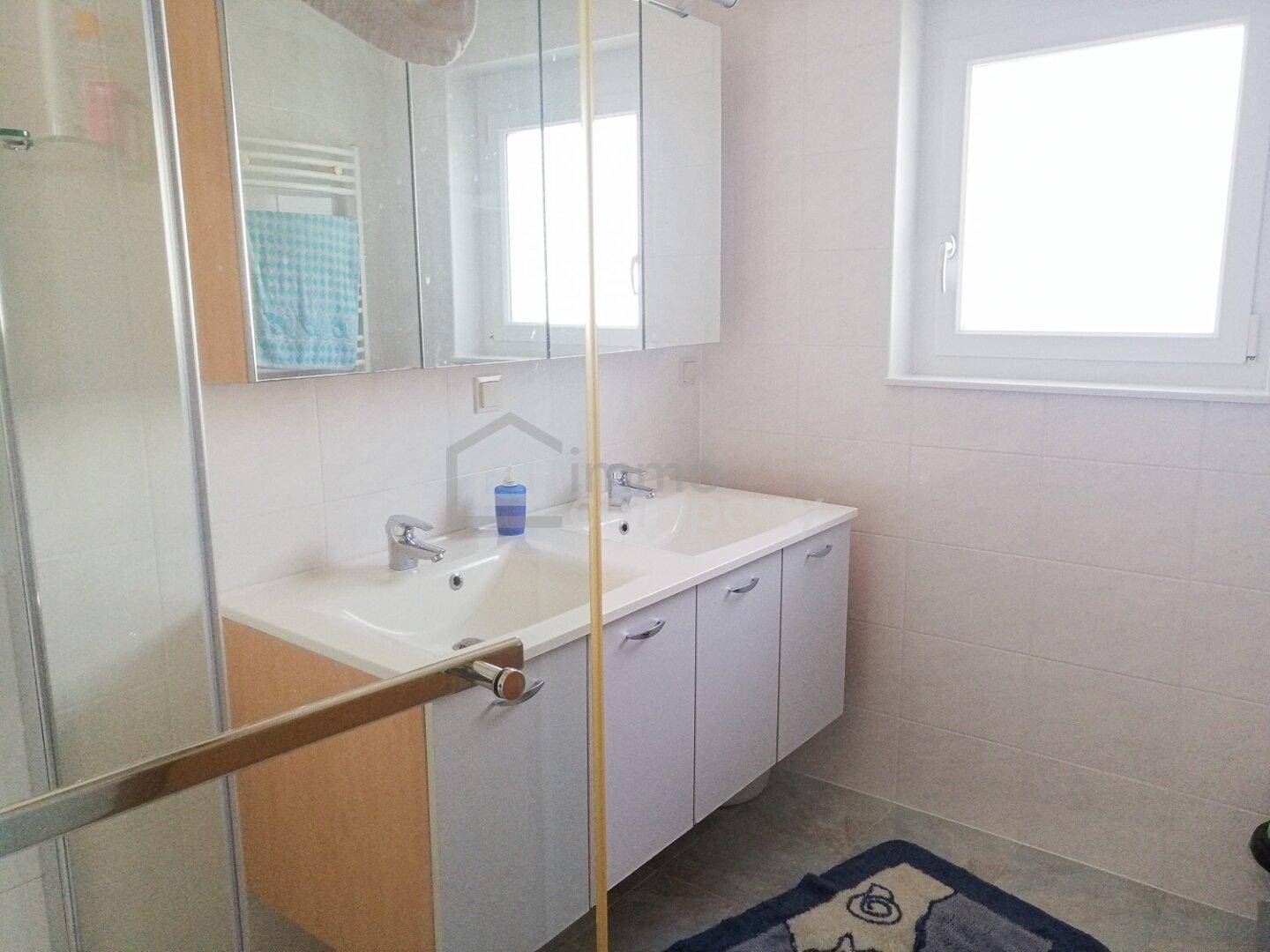 Modernes Badezimmer mit Doppelwaschbecken, Spiegelschrank und Fenster für Tageslicht.