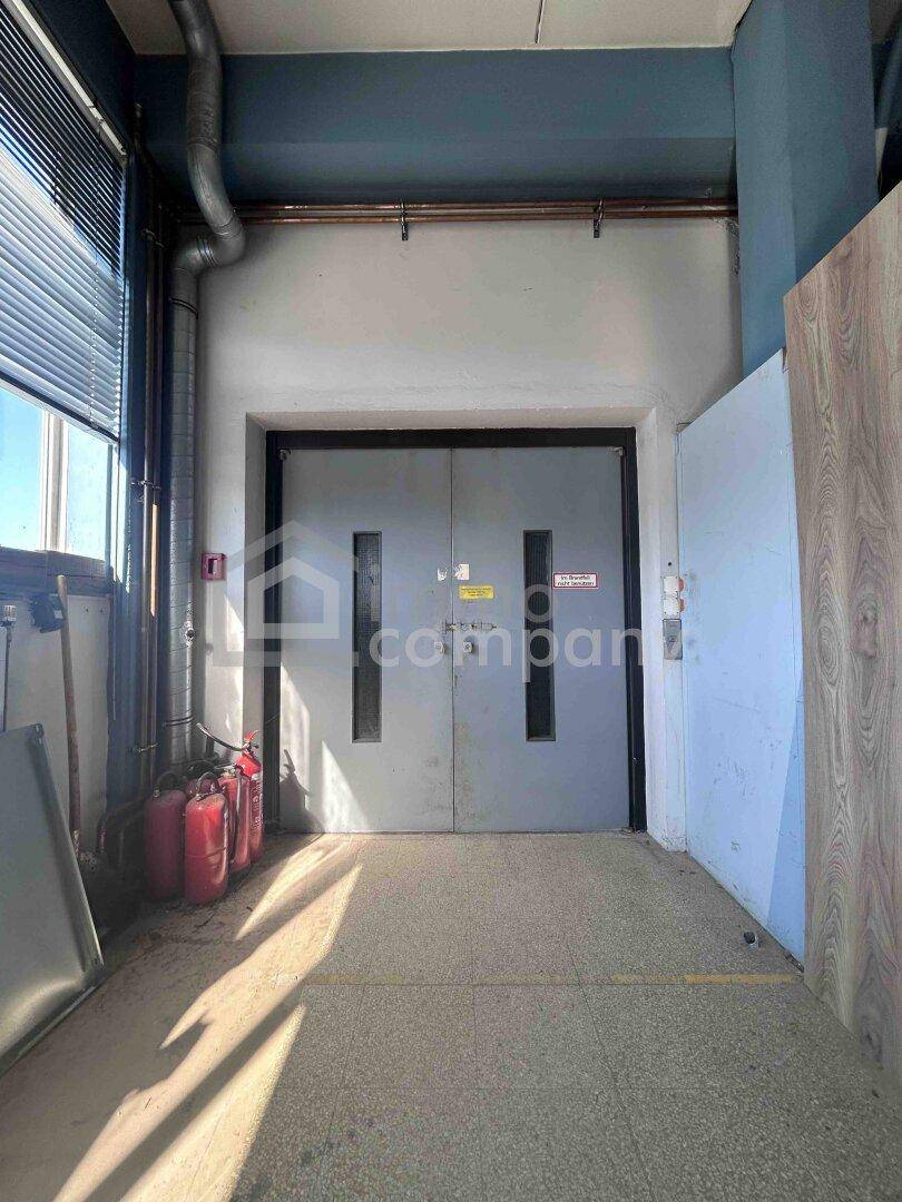 Große Doppeltür, möglicherweise ein Lastenaufzug, in einem Flur mit Feuerlöschern und Fenster.