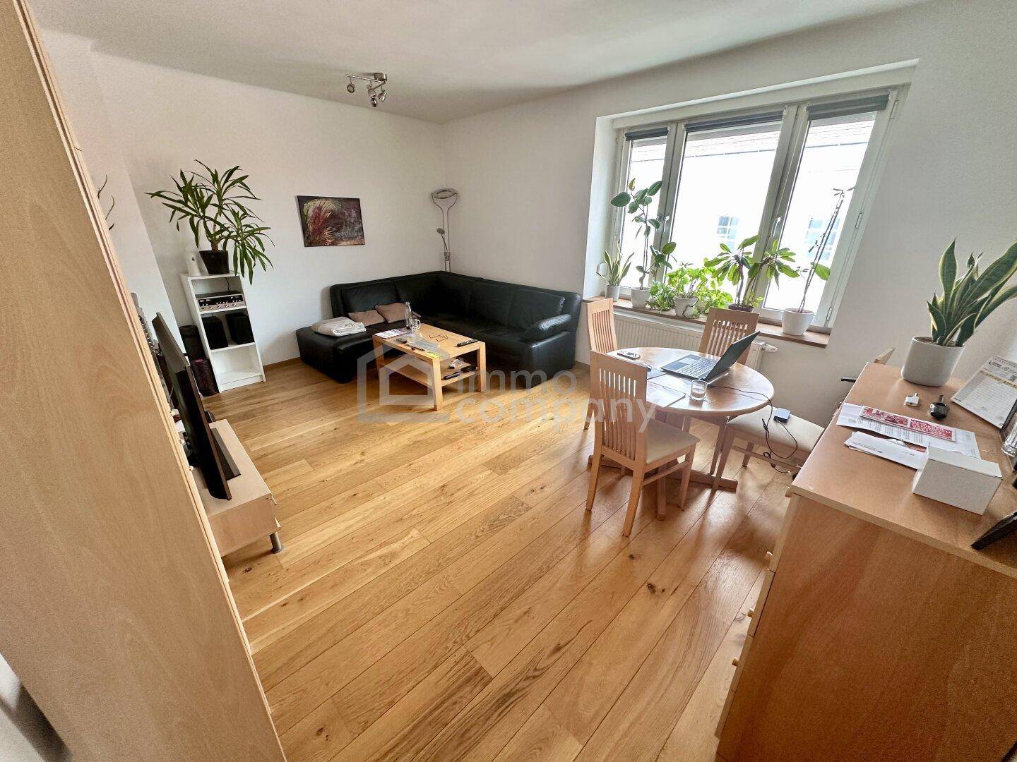 Heller Wohn- und Essbereich mit Holzboden, großem Fenster und gemütlicher Sitzecke.