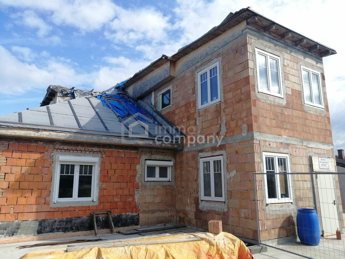 Haus im Rohbau mit sichtbaren Ziegelwänden und neuen Fenstern, das Dach ist teilweise abgedeckt.