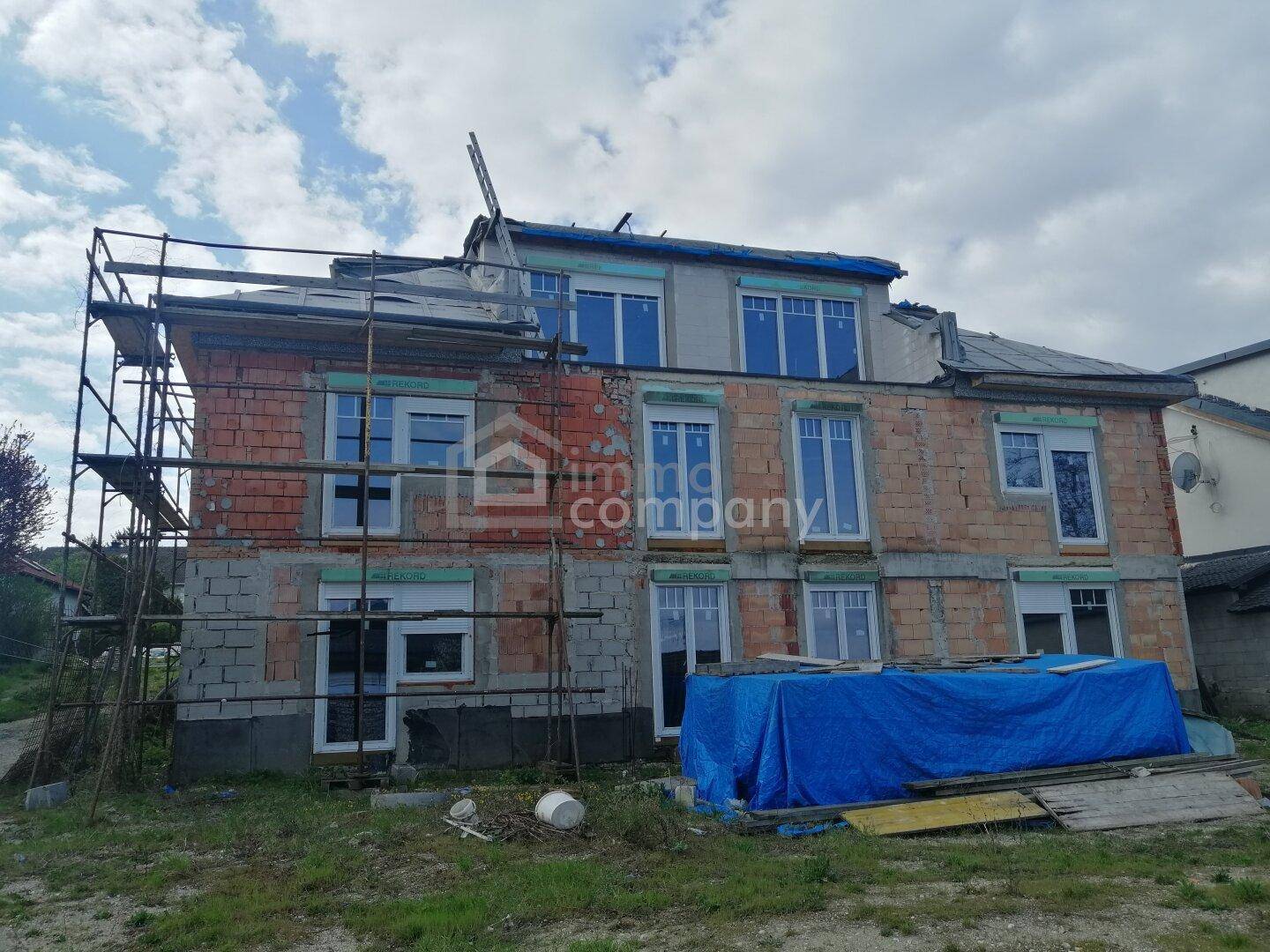 Im Bau befindliches Gebäude mit Gerüst, sichtbaren Ziegelwänden und bereits installierten Fenstern.