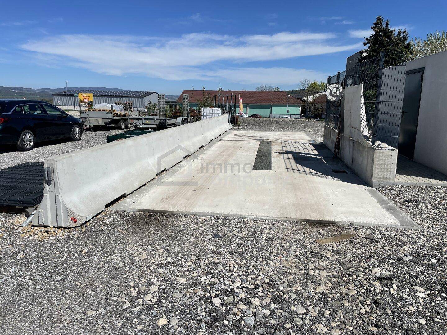 Außenbereich mit Betonbarrieren und einer befestigten Fläche, möglicherweise für Fahrzeugwartung oder -reinigung.