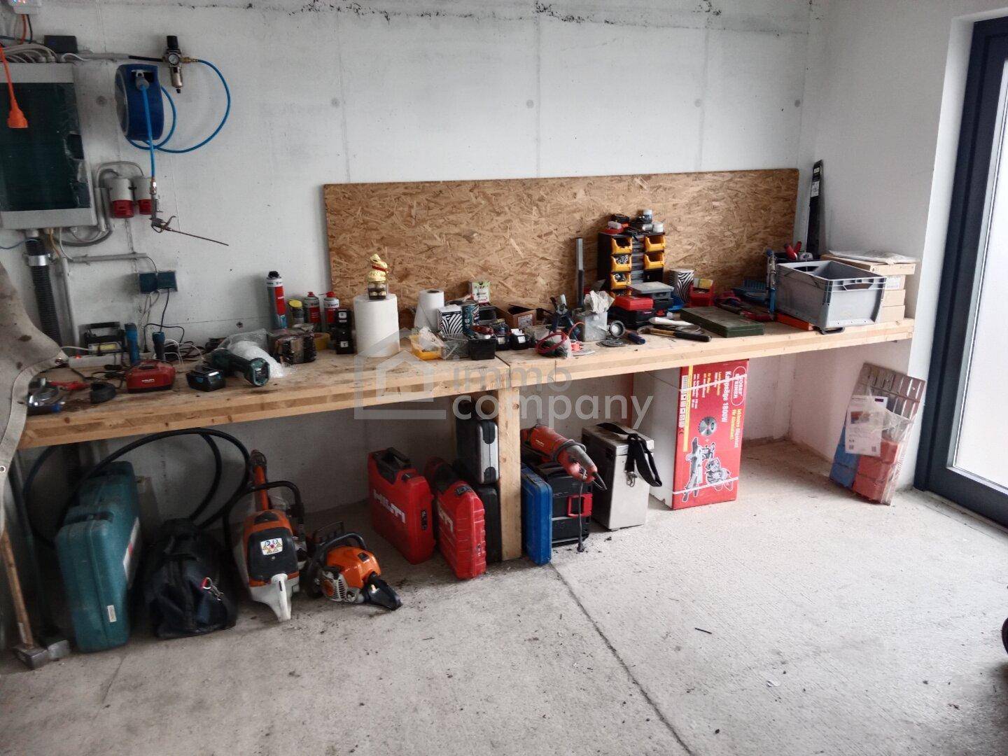 Werkstattraum mit einer langen Holzwerkbank, vielen Werkzeugen und einer Betonwand, ideal für handwerkliche Arbeiten.