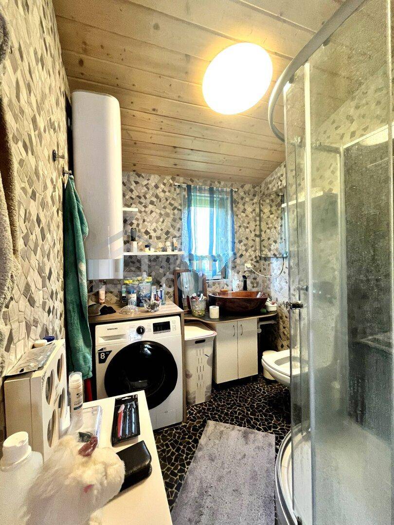 Badezimmer mit Duschkabine, Waschmaschine und gemusterten Wänden unter einer Holzdecke.