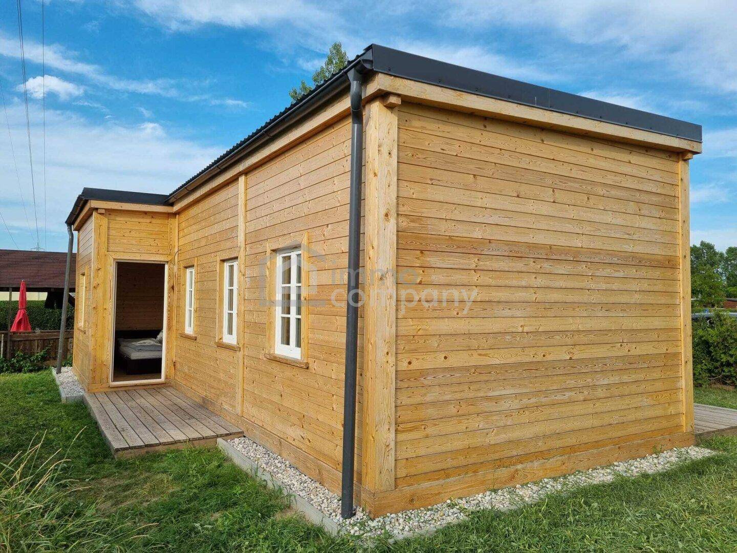 Kleines Holzhaus mit einfacher Architektur und weiß gerahmten Fenstern unter blauem Himmel.