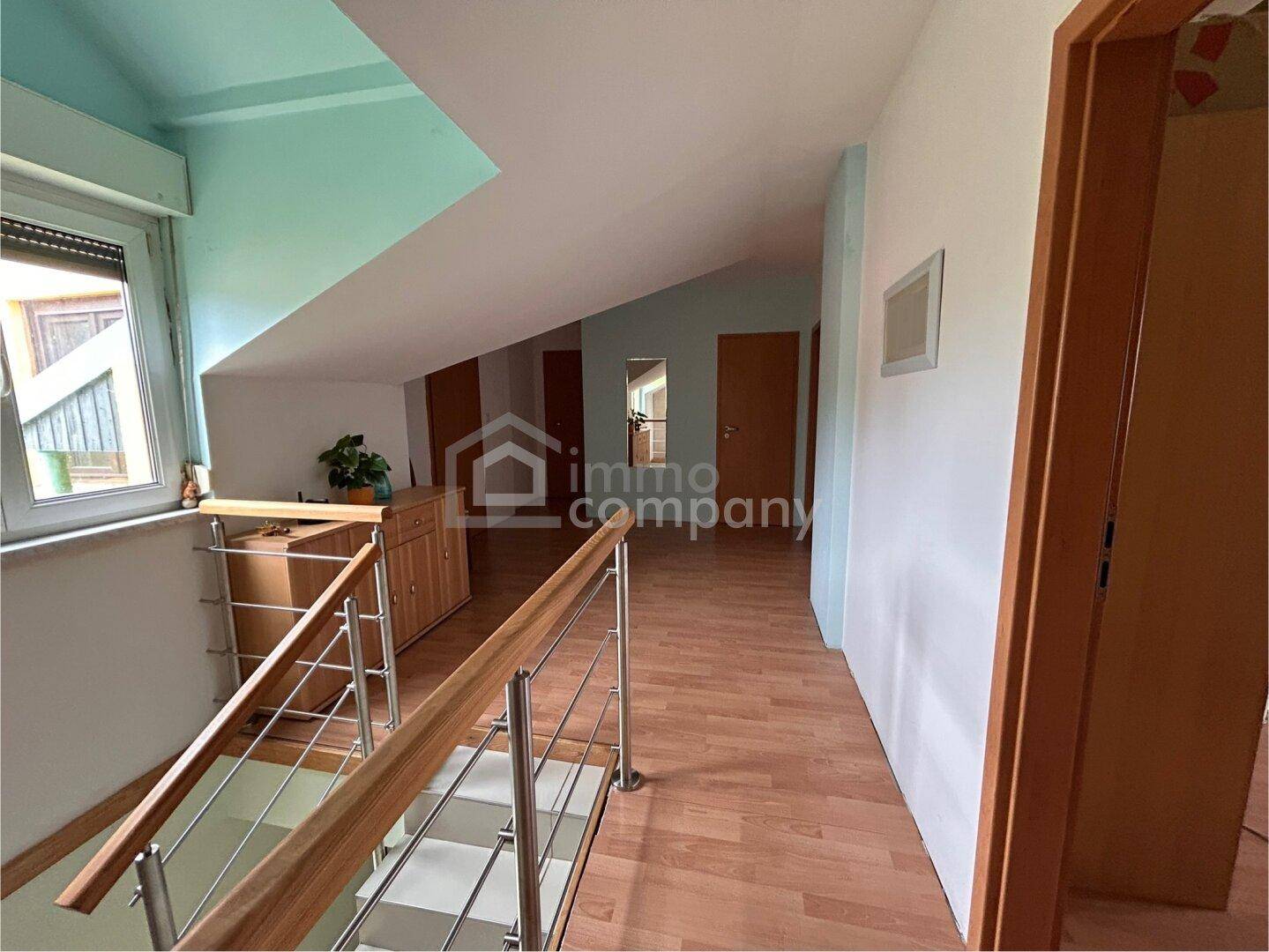 Heller Flur im Dachgeschoss mit Holztreppe, Laminatboden und mehreren Türen.