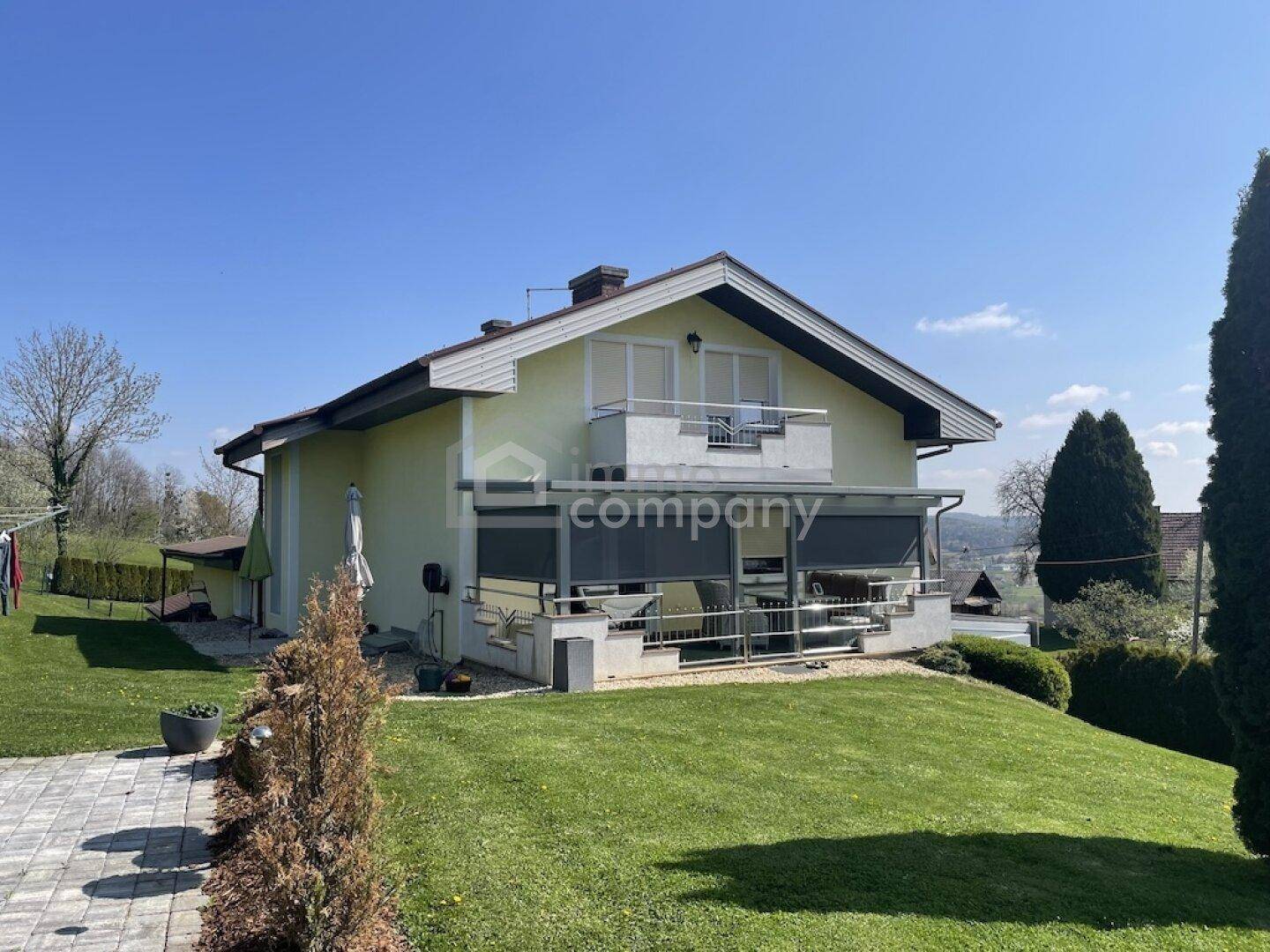 Rückansicht des Hauses mit Balkon, überdachter Terrasse und weitläufigem Rasen.