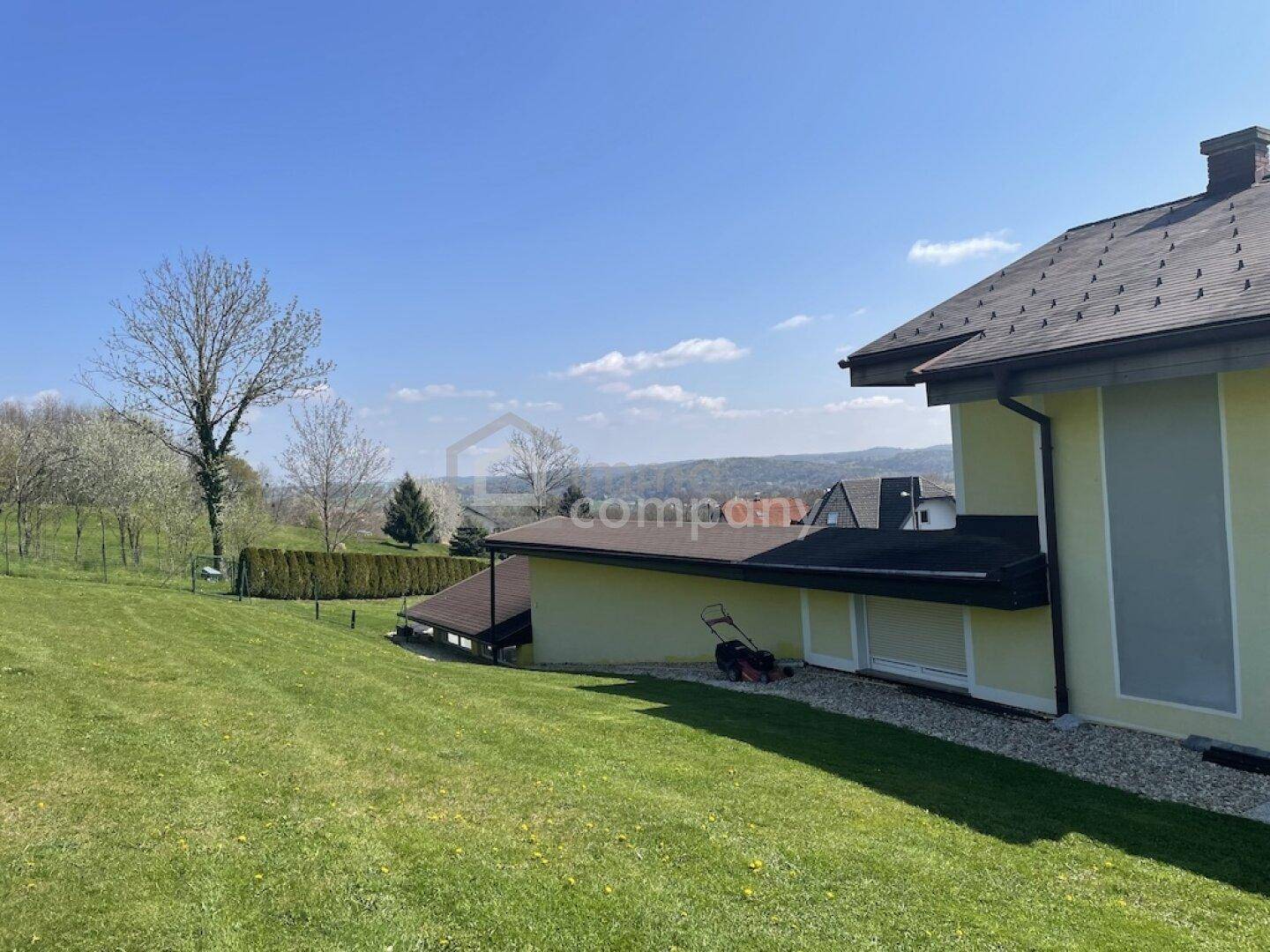 Seitenansicht des Hauses mit abfallendem Rasen und Blick auf die umliegende Natur.