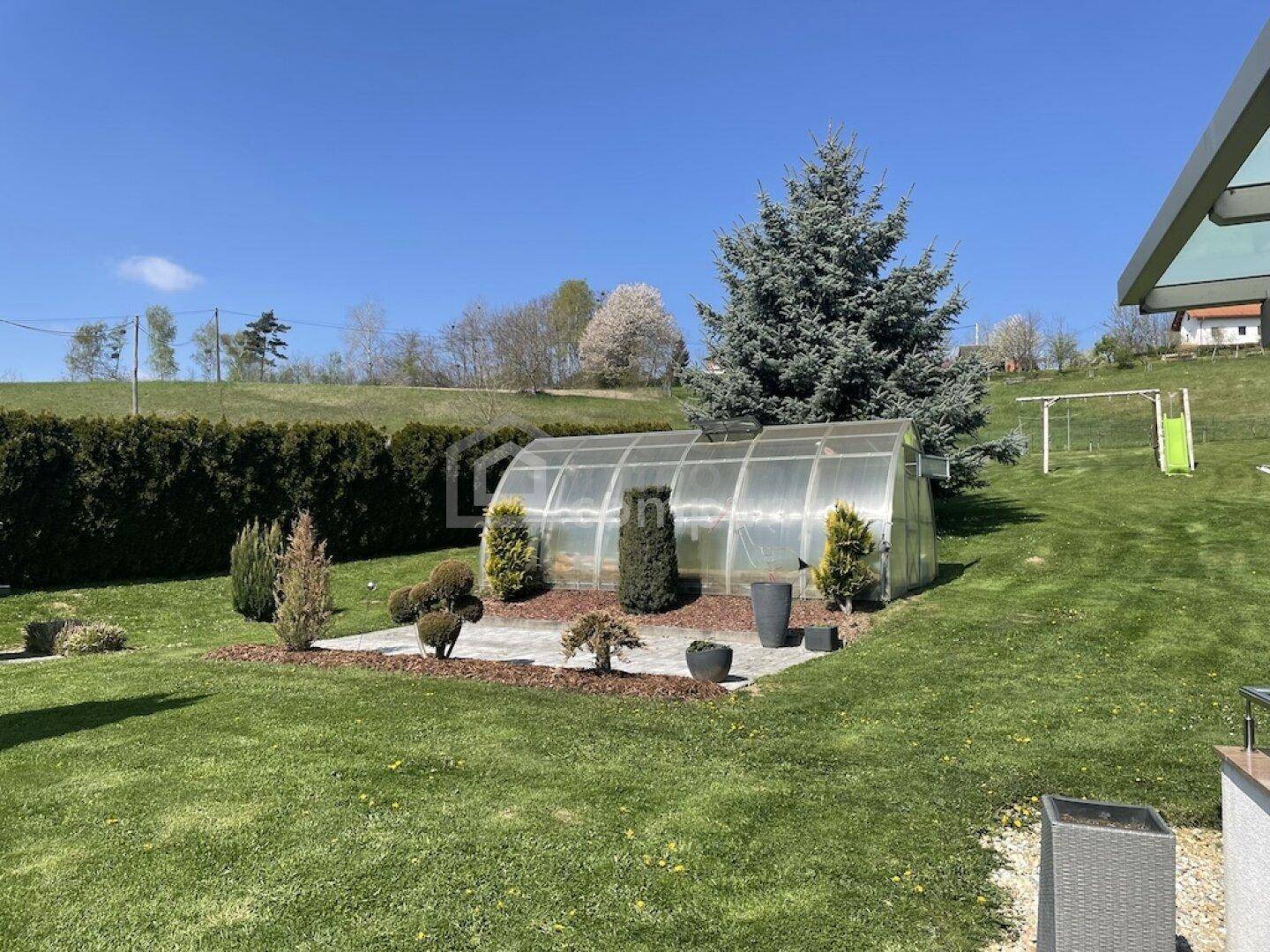 Garten mit Gewächshaus, großem Baum und einem kleinen Spielplatz im Hintergrund.