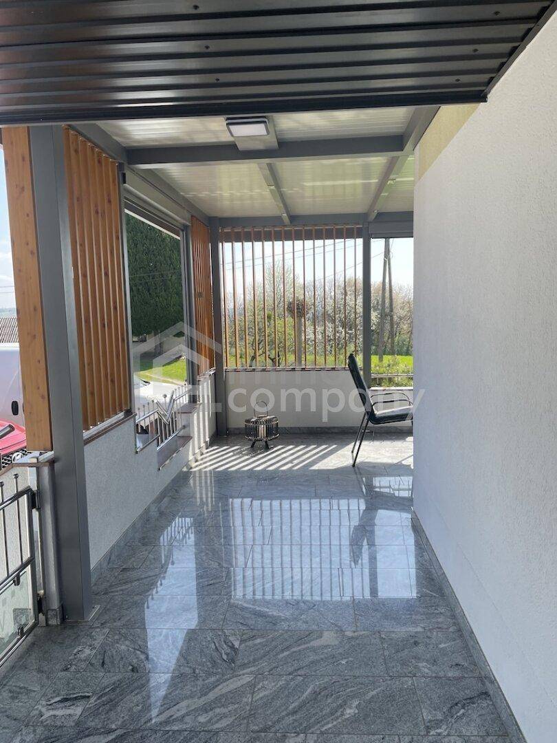 Überdachte Terrasse mit glänzendem Fliesenboden und Blick ins Grüne.