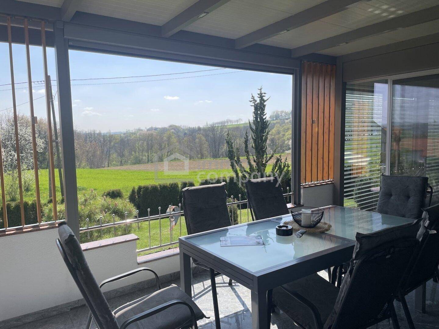 Gemütliche überdachte Terrasse mit Esstisch und Stühlen, bietet weite Aussicht.