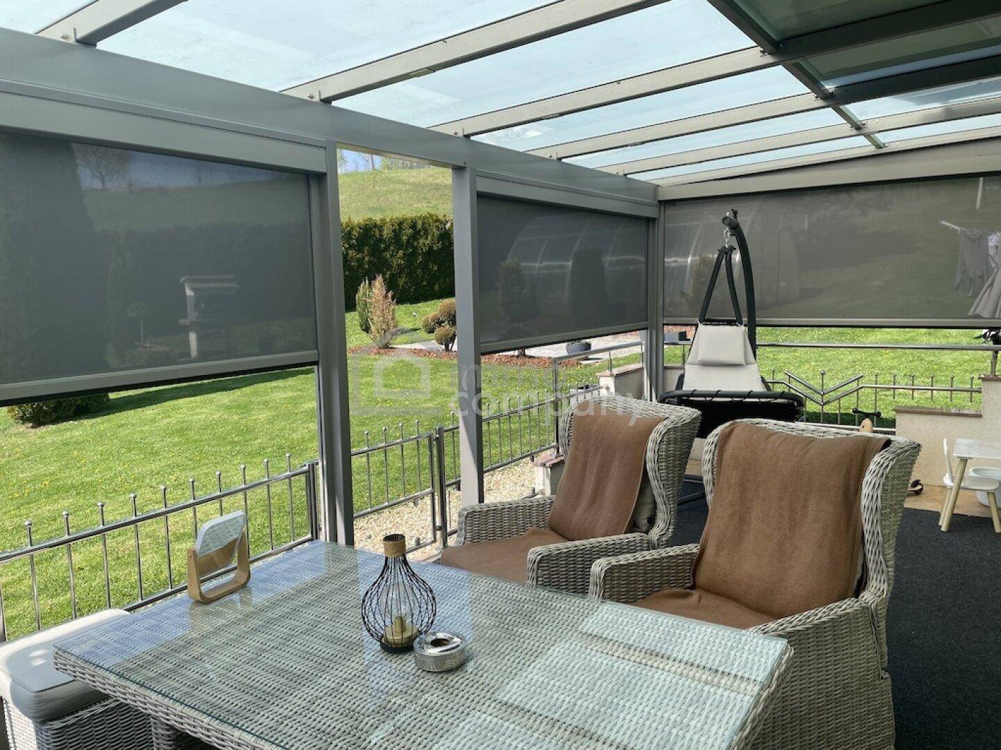 Gemütliche überdachte Terrasse mit Rattanmöbeln und Blick ins Grüne.