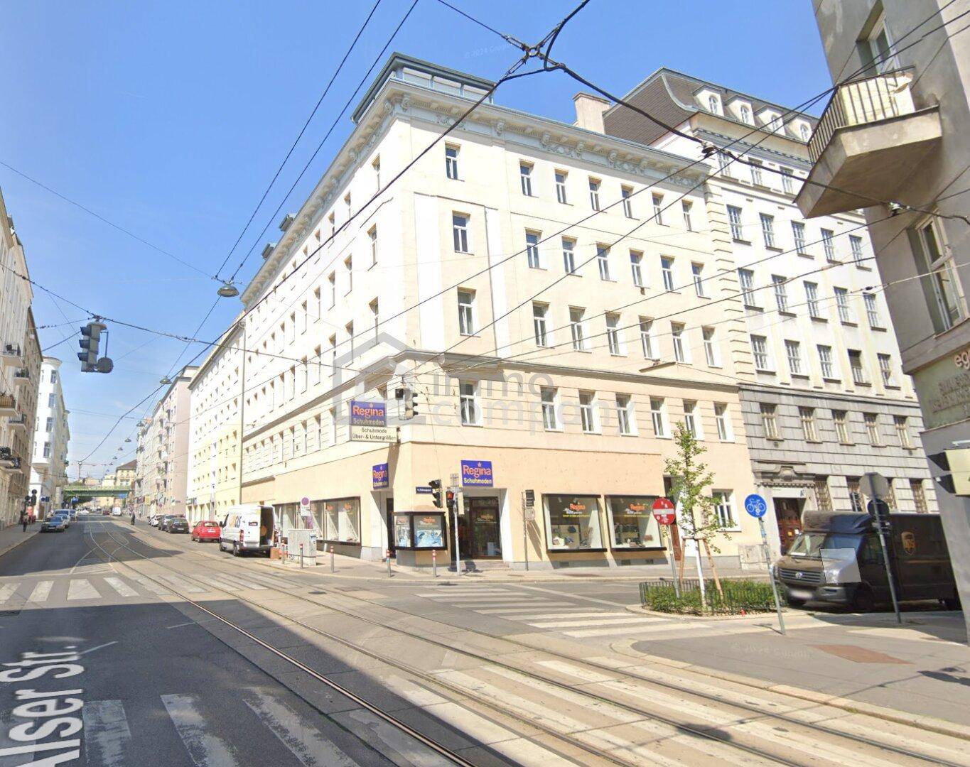 Historisches Eckgebäude in urbaner Umgebung mit Geschäften im Erdgeschoss und Straßenbahnschienen davor.