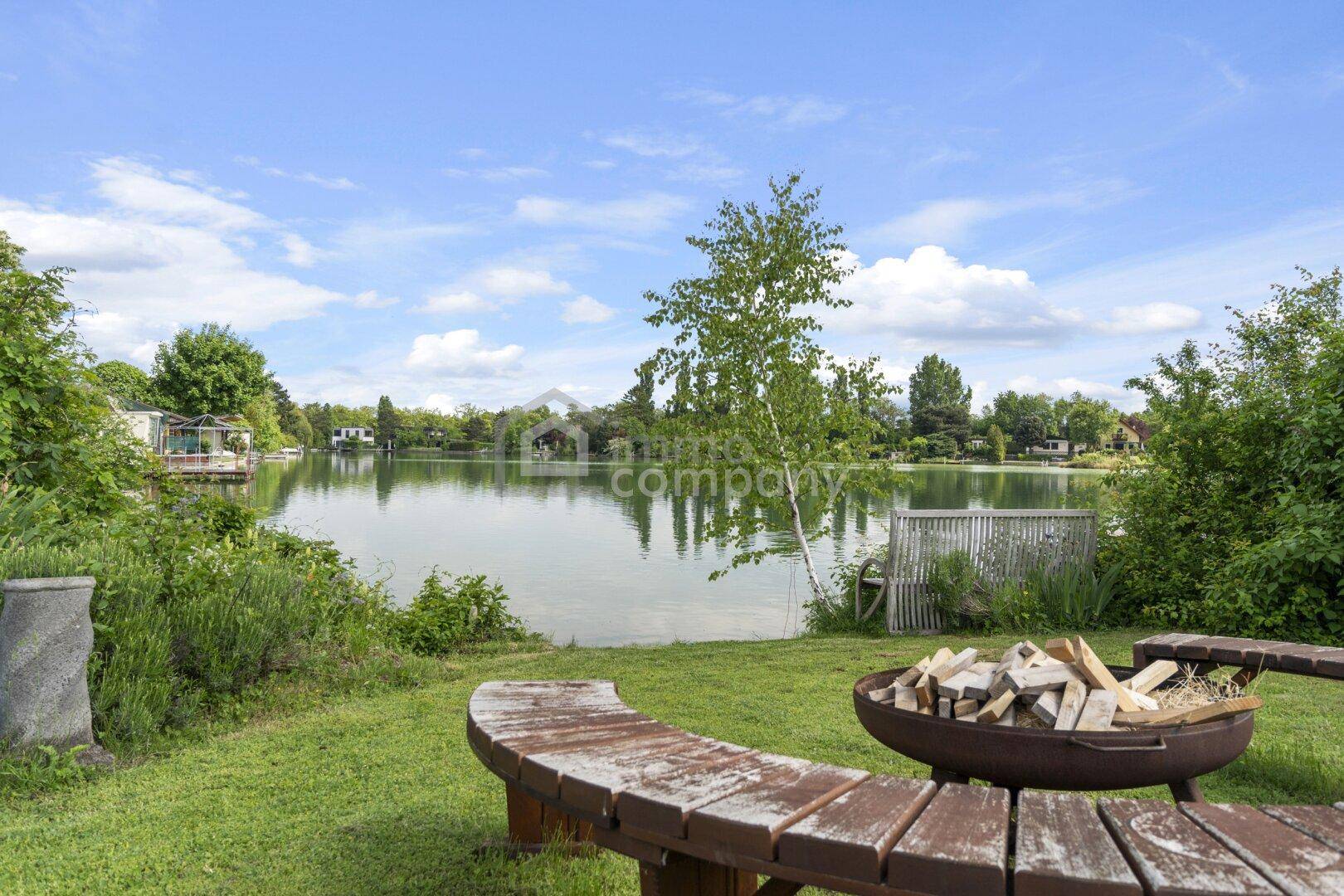 Idyllischer Gartenbereich am Seeufer mit Feuerstelle und rustikaler Holzbank.