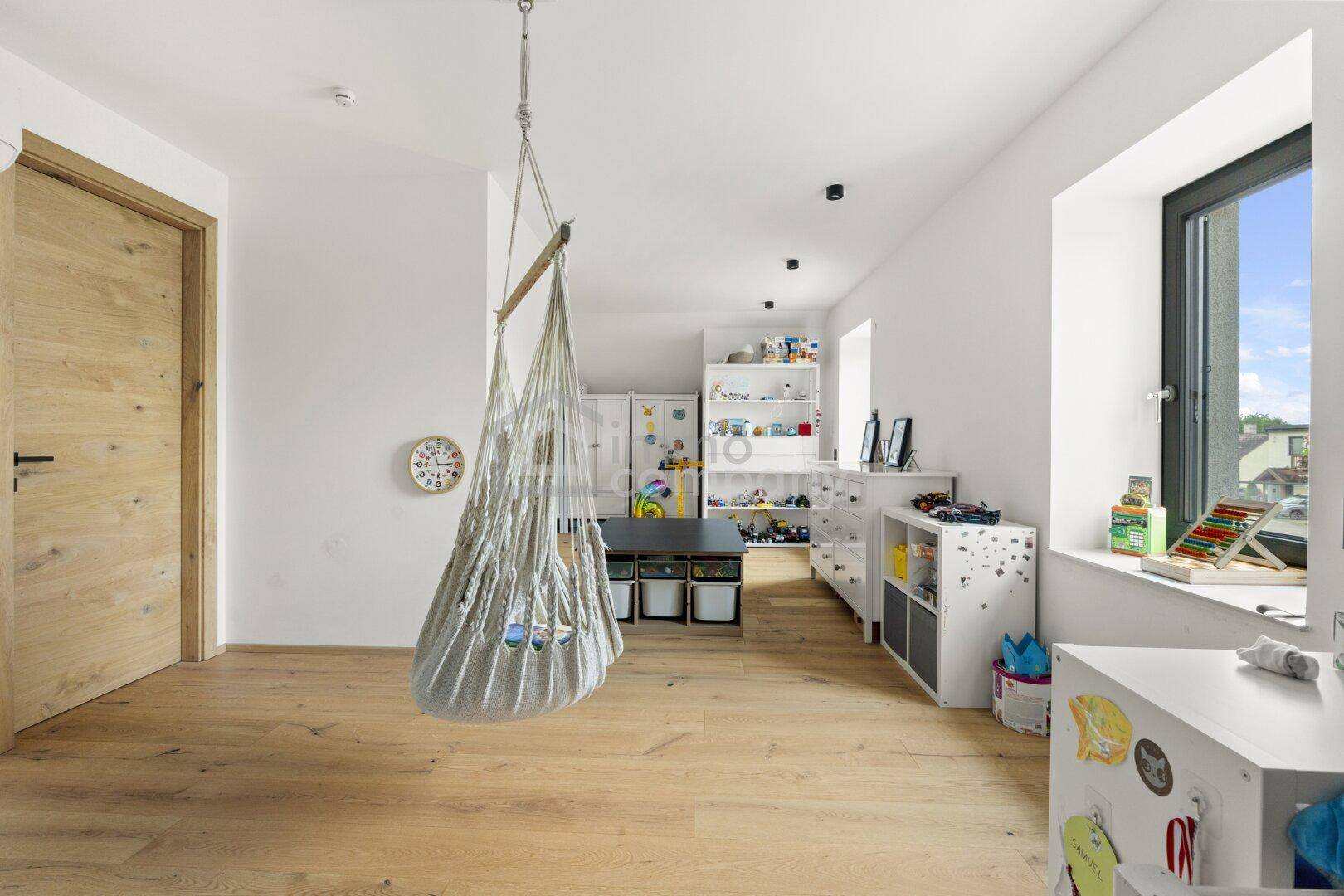 Geräumiges Kinderzimmer mit Holzboden, Schaukel und viel Stauraum für Spielzeug.