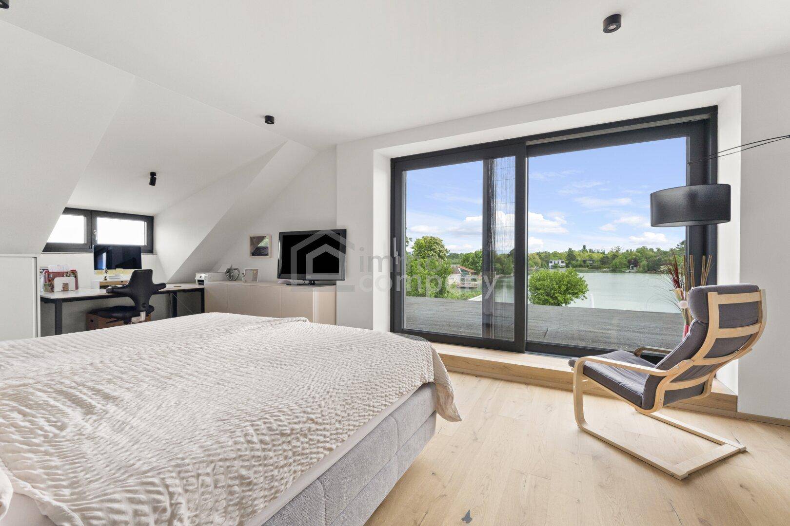 Helles Schlafzimmer mit Seeblick, Holzboden, Schreibtisch und Zugang zu einem Balkon.