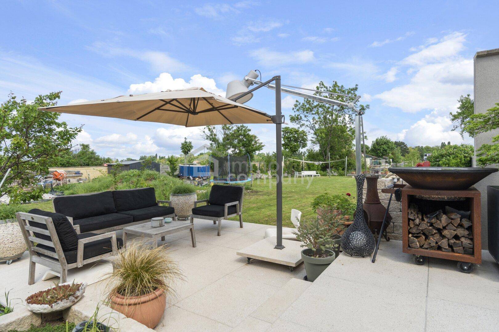 Gepflasterte Terrasse mit bequemen Gartenmöbeln, Sonnenschirm und Blick in den Garten.
