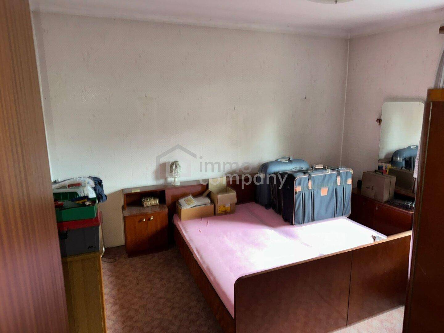 Ein weiteres Schlafzimmer mit einem Bett und einfachen Möbeln, das Renovierungsbedarf aufweist.