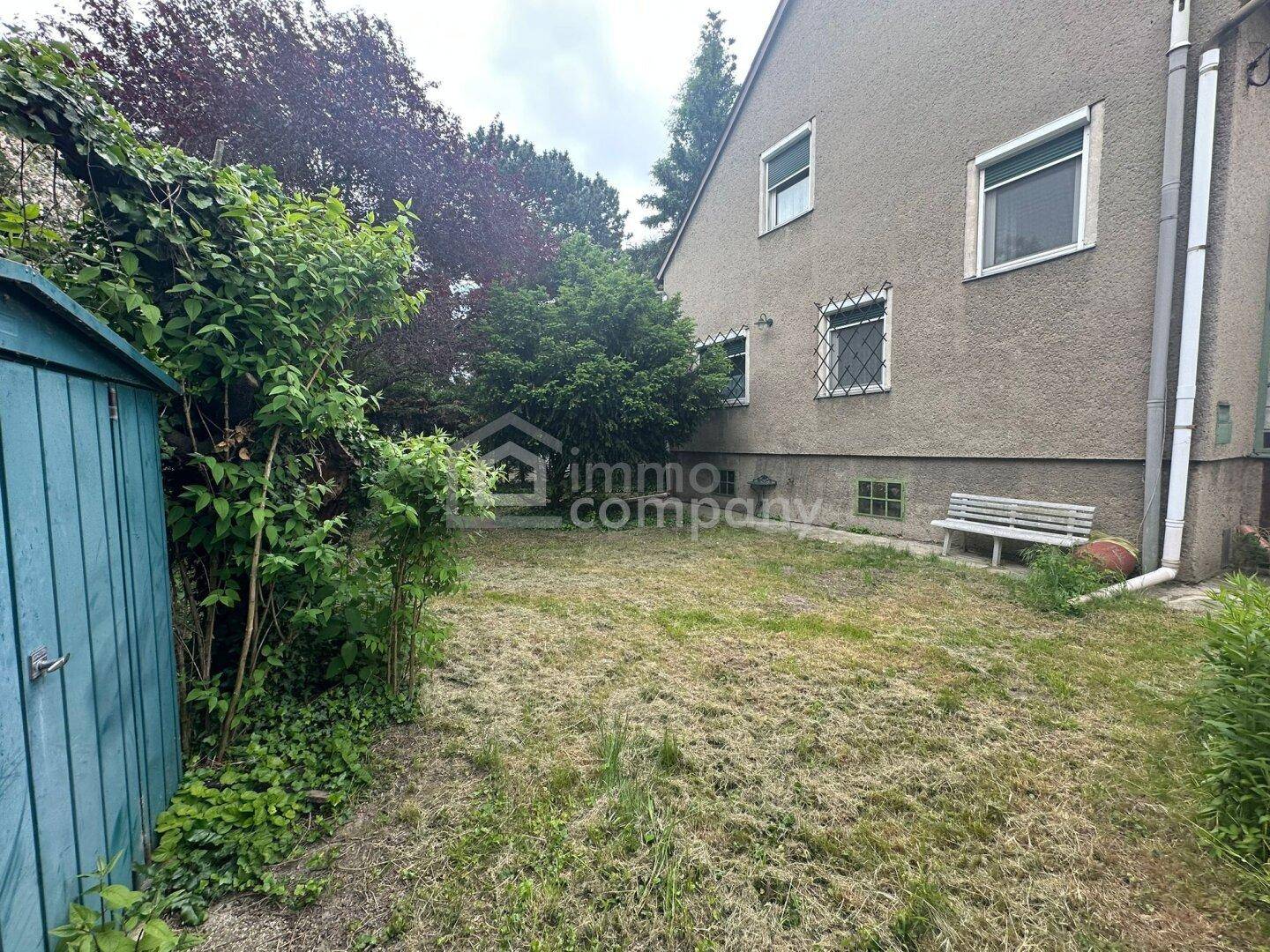 Der Gartenbereich hinter dem Haus mit Rasenfläche, Sträuchern und einem kleinen Geräteschuppen.