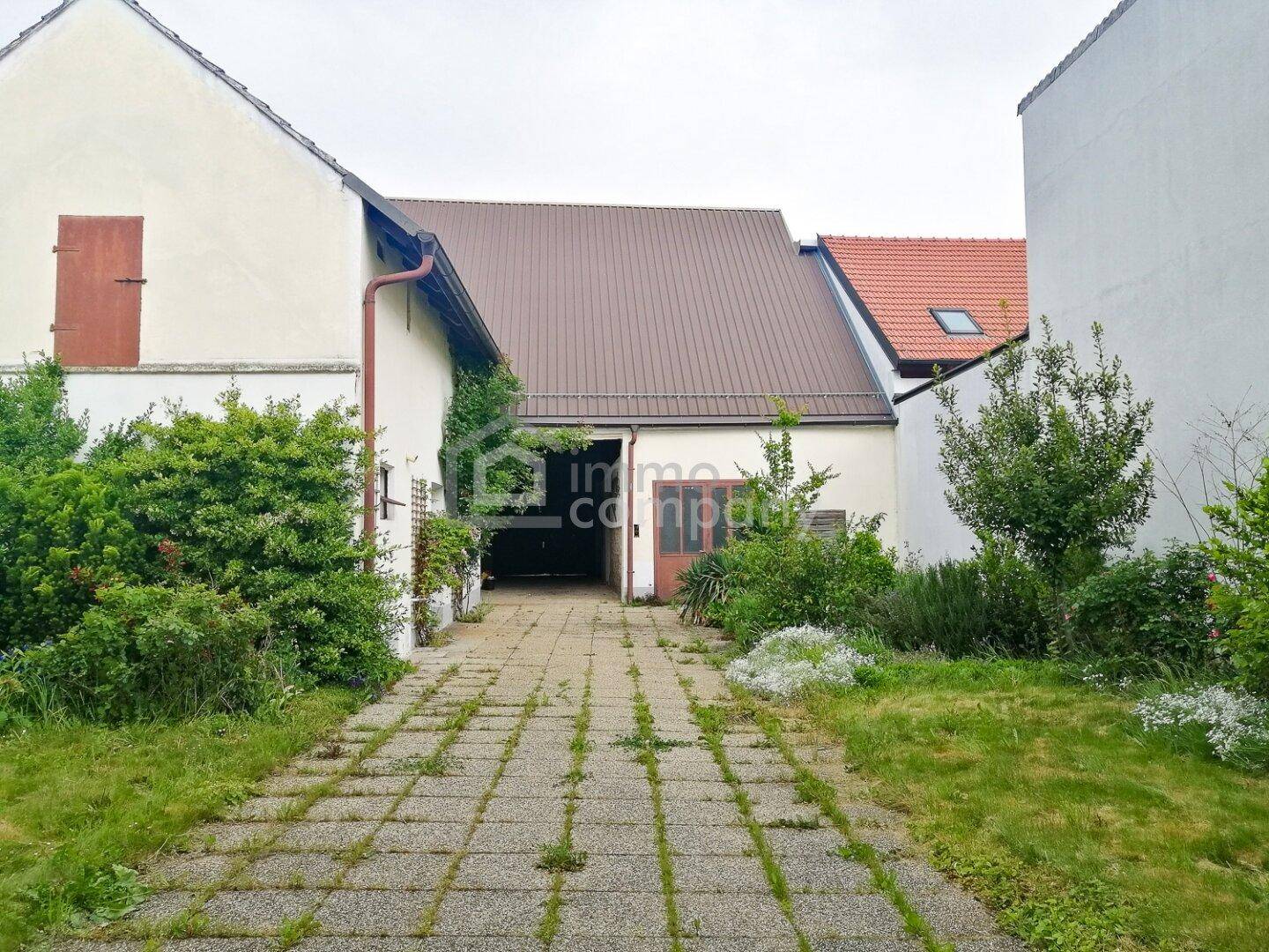 Ungepflegter Hofbereich mit gepflastertem Weg und offenem Zugang zu einer Scheune.