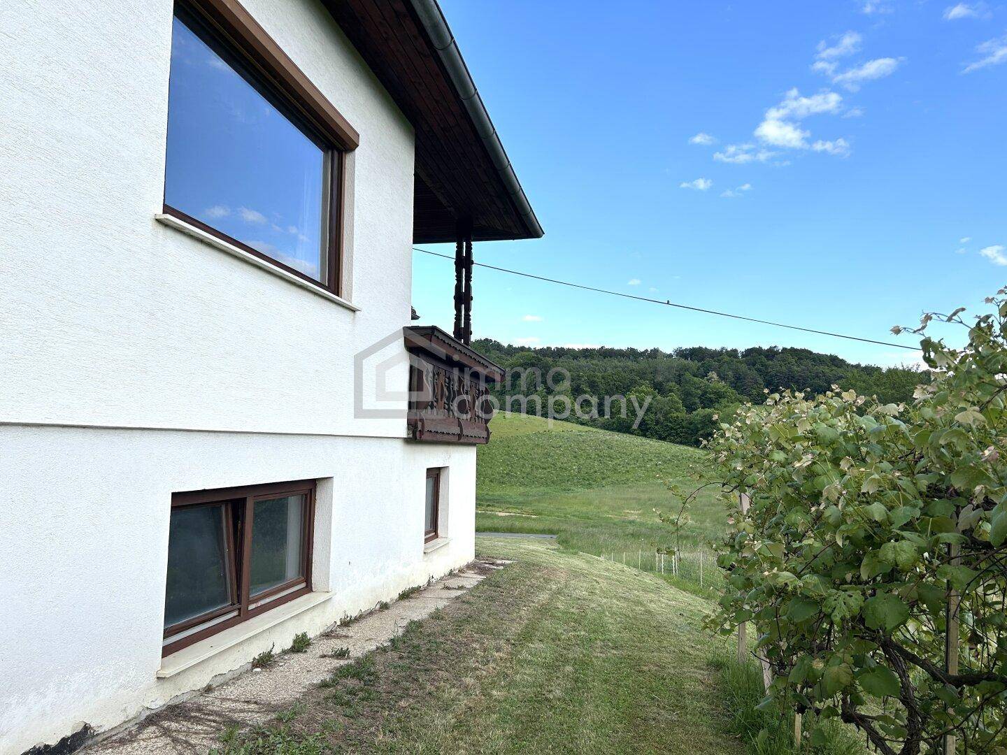 Seitenansicht des Hauses mit Fenstern und Blick auf die hügelige, grüne Landschaft.