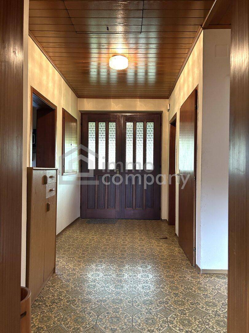 Langer Flur mit gemustertem Fliesenboden und Holzdecke, führt zum Eingangsbereich.