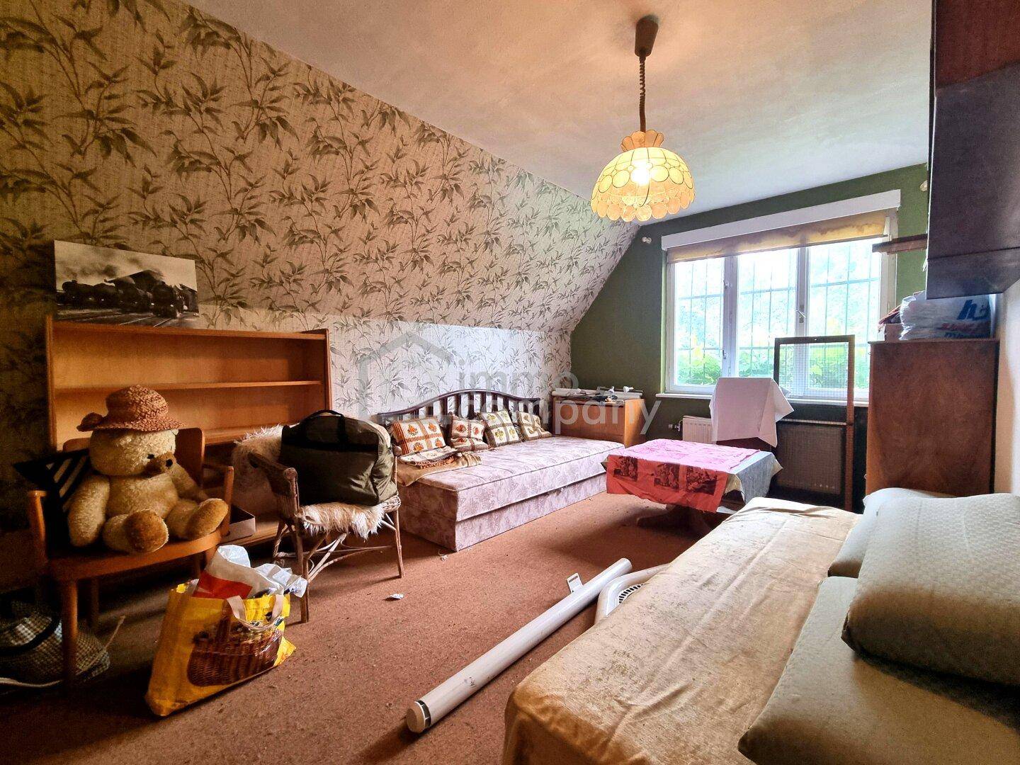 Gemütliches Dachzimmer mit schräger Decke, floraler Tapete und einem Tagesbett.