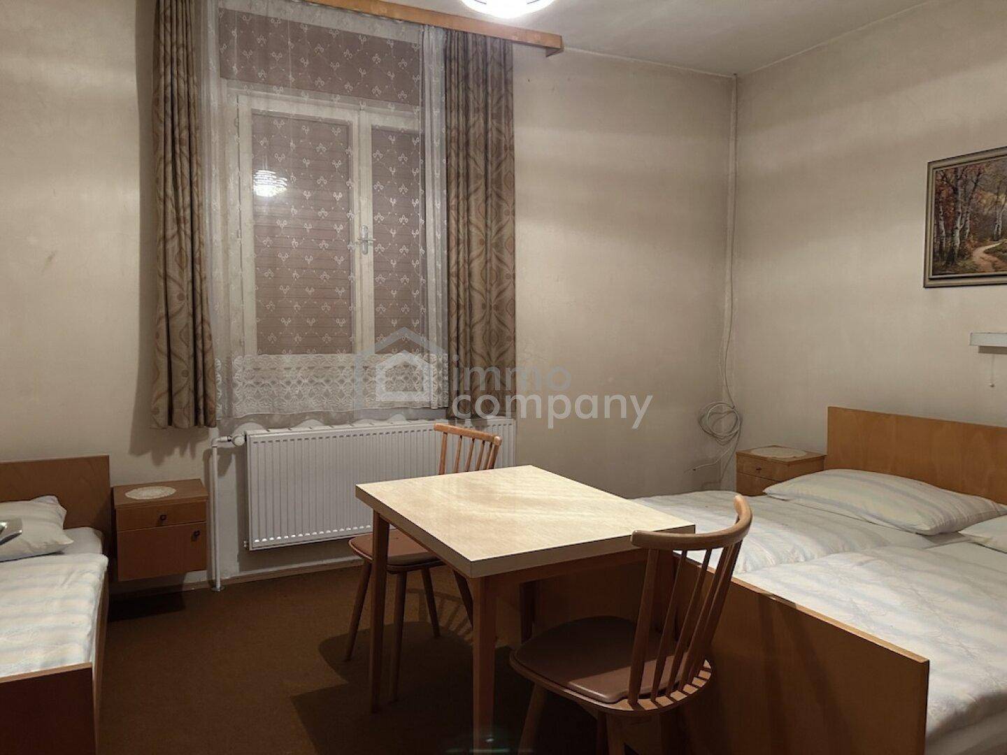 Schlafzimmer mit zwei Betten und einem Tisch, ausgestattet mit Vorhängen und Heizung.