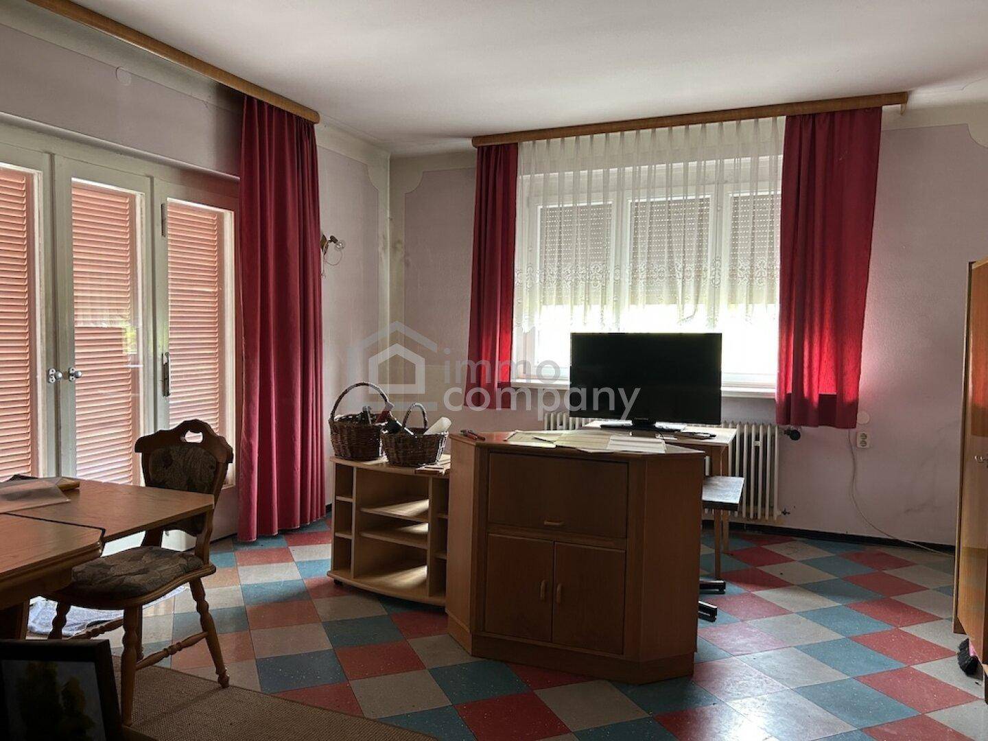 Wohnzimmer mit farbenfrohem Fliesenboden, großen Fenstern und Zugang zum Außenbereich.