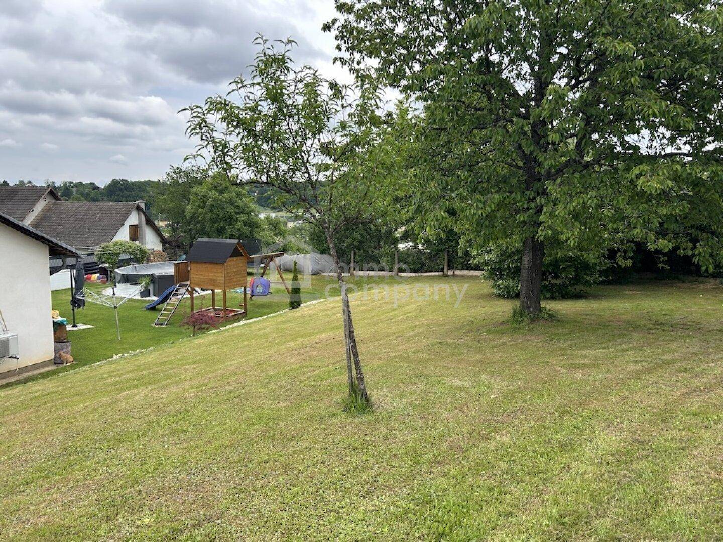 Großer Garten mit Rasenfläche, Bäumen und Kinderspielplatz, ideal für Familien.