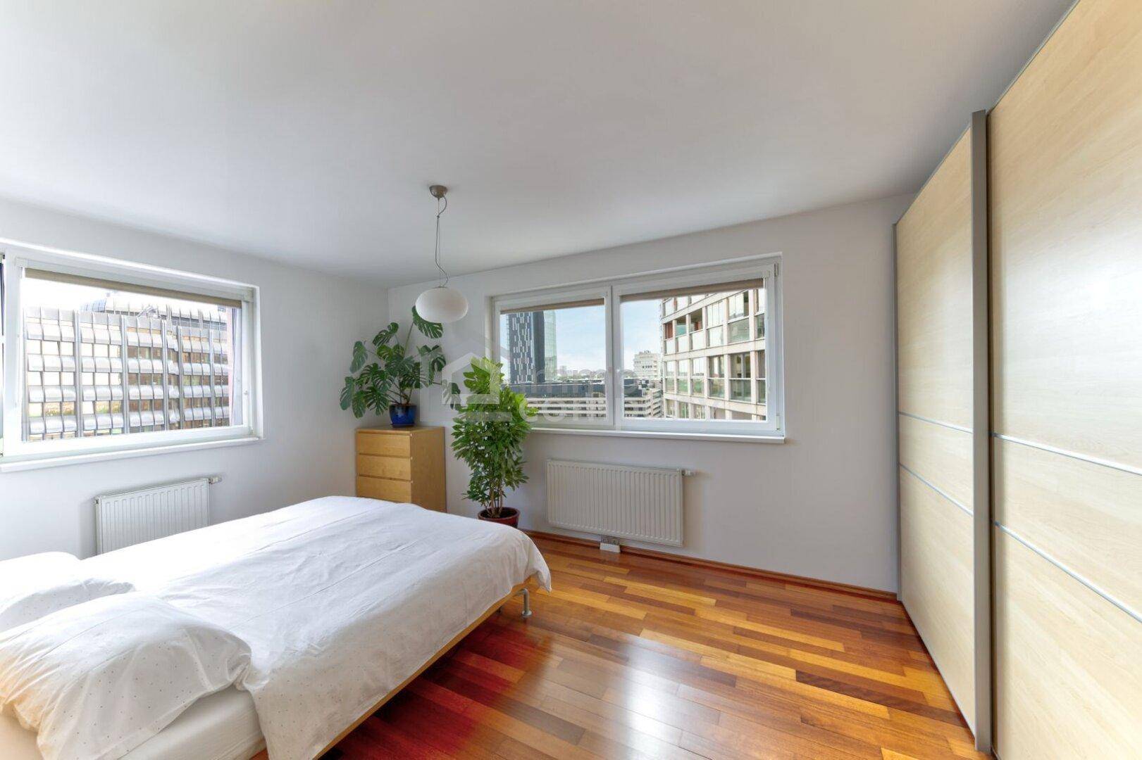 Helles Schlafzimmer mit Holzboden, Einbauschränken und Blick auf die Stadt.