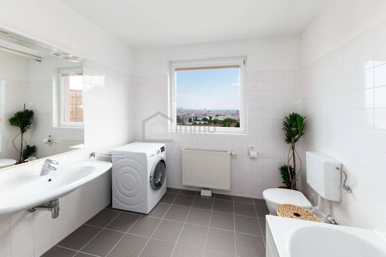 Funktionales Badezimmer mit Badewanne, Waschbecken, Fenster und Stadtblick.