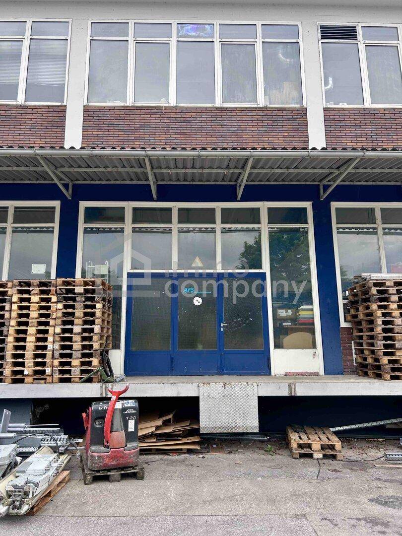 Außenansicht des Gebäudes mit Laderampe, blauer Tür und großen Fenstern im Obergeschoss.