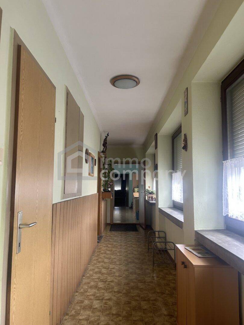 Langer Flur mit hellgrünen Wänden, Holzvertäfelung und Fliesenboden, der zu weiteren Räumen führt.