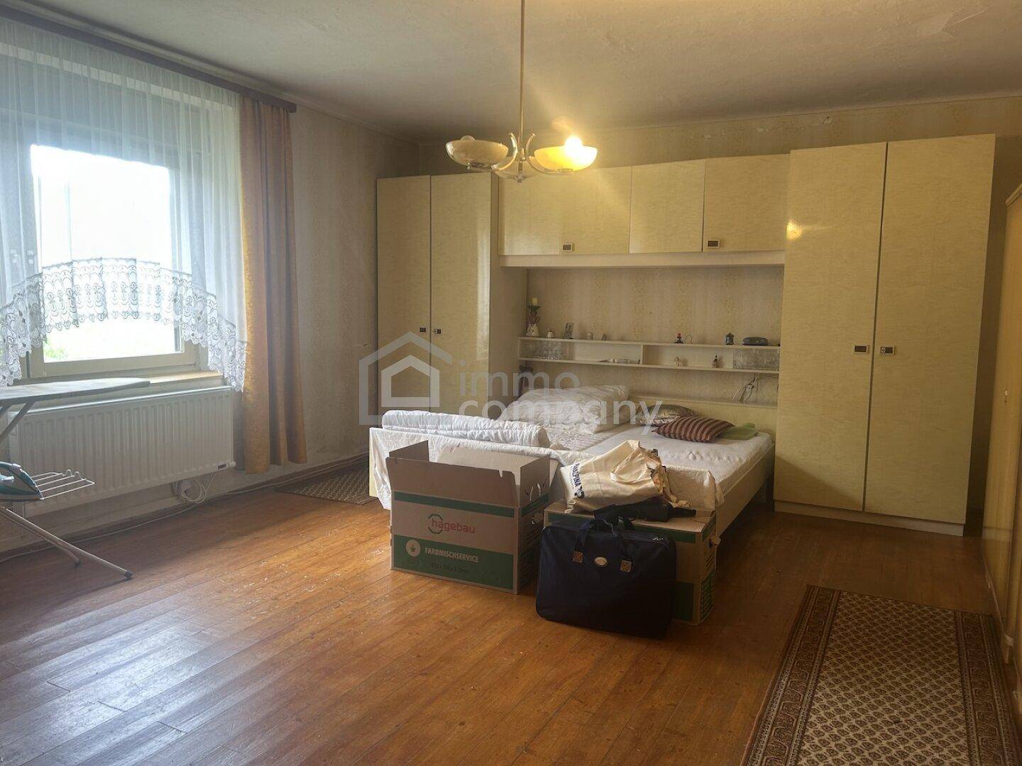 Schlafzimmer mit Holzboden, Einbauschränken und einem Fenster, das Tageslicht hereinlässt.