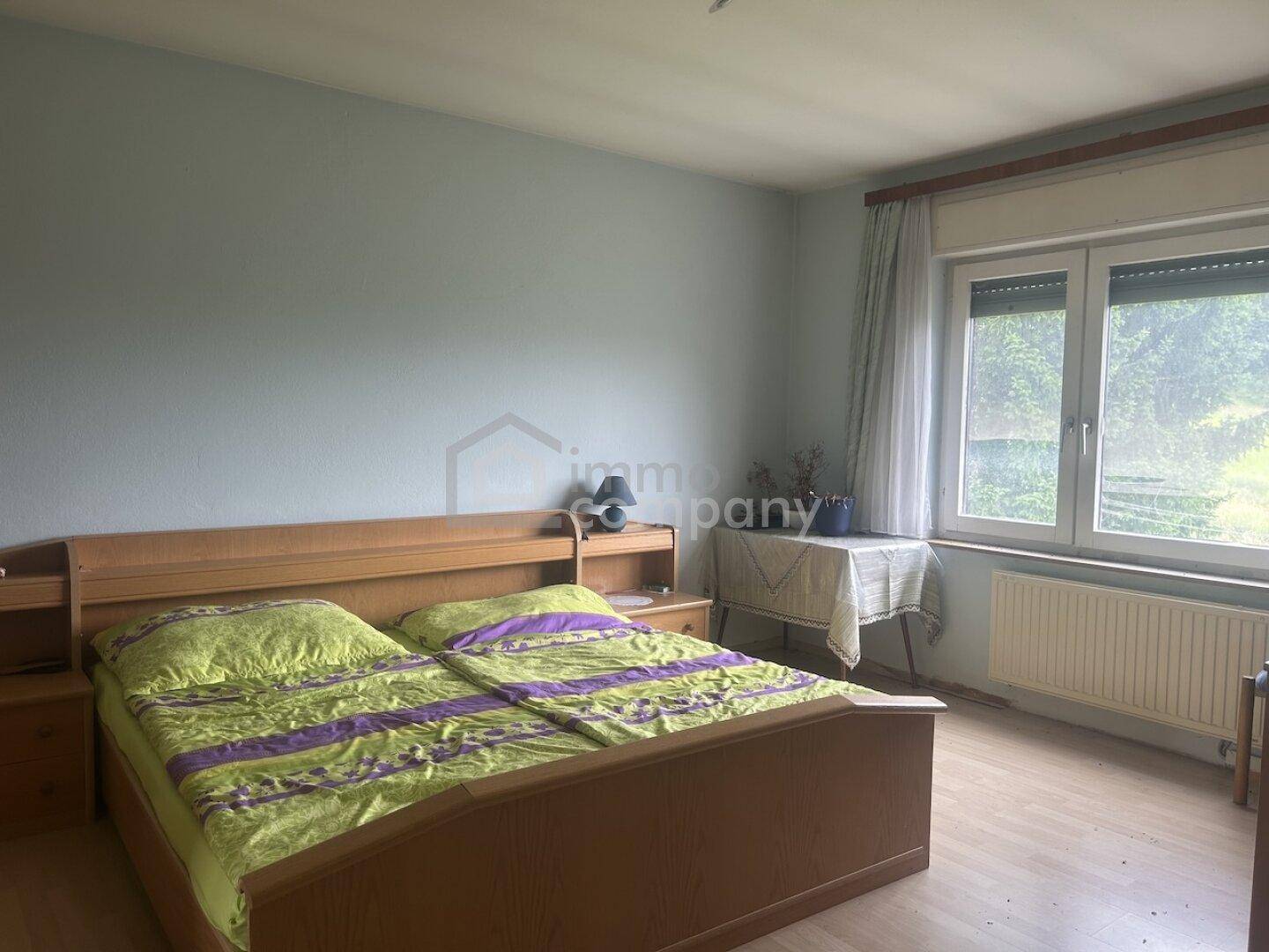 Helles Schlafzimmer mit Doppelbett, Nachttischen und Blick ins Grüne durch das Fenster.