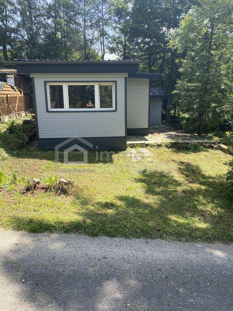 Ansicht des kleinen Hauses von der Straße mit gepflegtem Rasen und Bäumen.