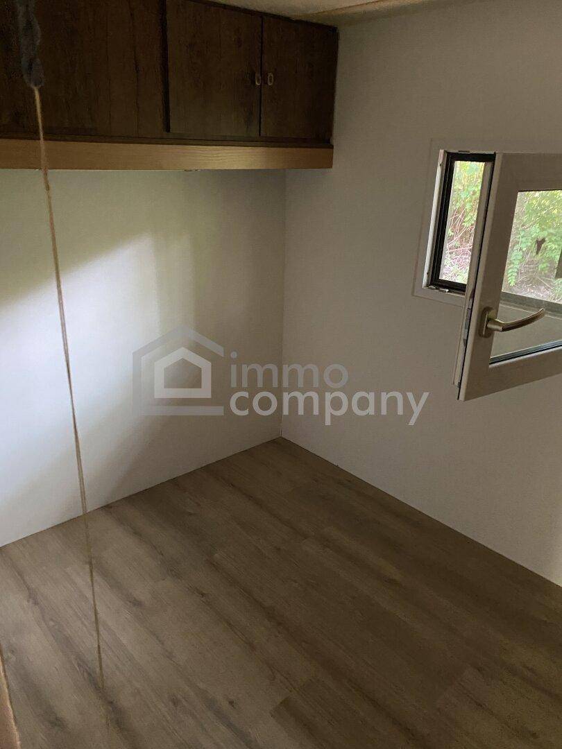 Kleiner, leerer Raum mit Laminatboden und einem Fenster, das viel Licht hereinlässt.