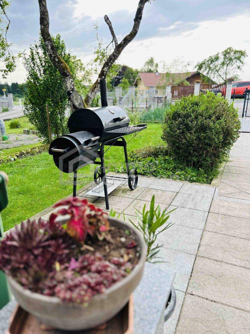 Detailansicht des Grills auf der gepflasterten Terrasse im grünen Gartenbereich.