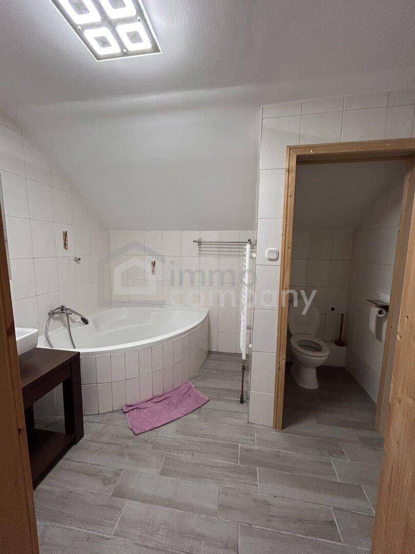 Helles Badezimmer mit Eckbadewanne, Fliesenboden und separatem WC-Bereich unter der Dachschräge.