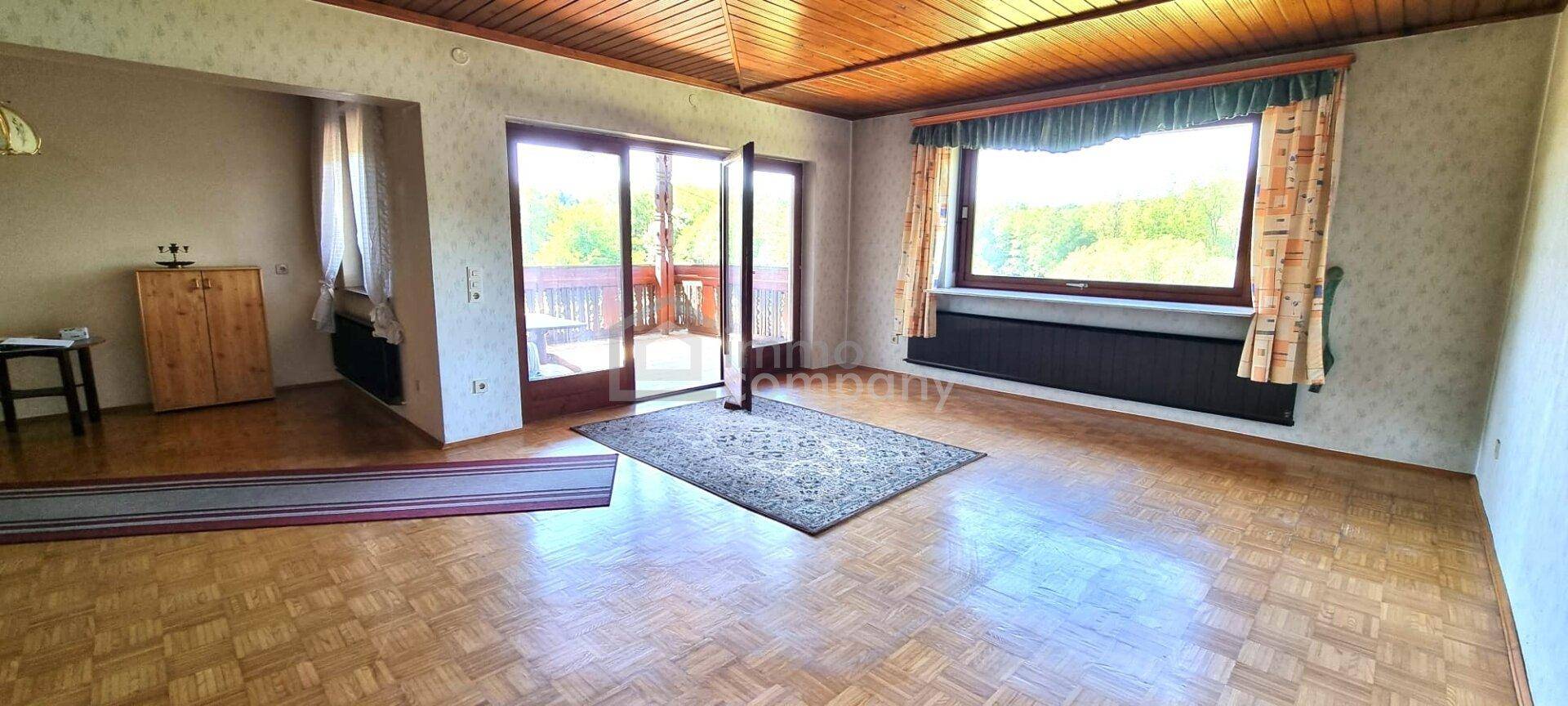 Geräumiges Wohnzimmer mit Parkettboden, Holzdecke und Zugang zum Balkon mit Aussicht.