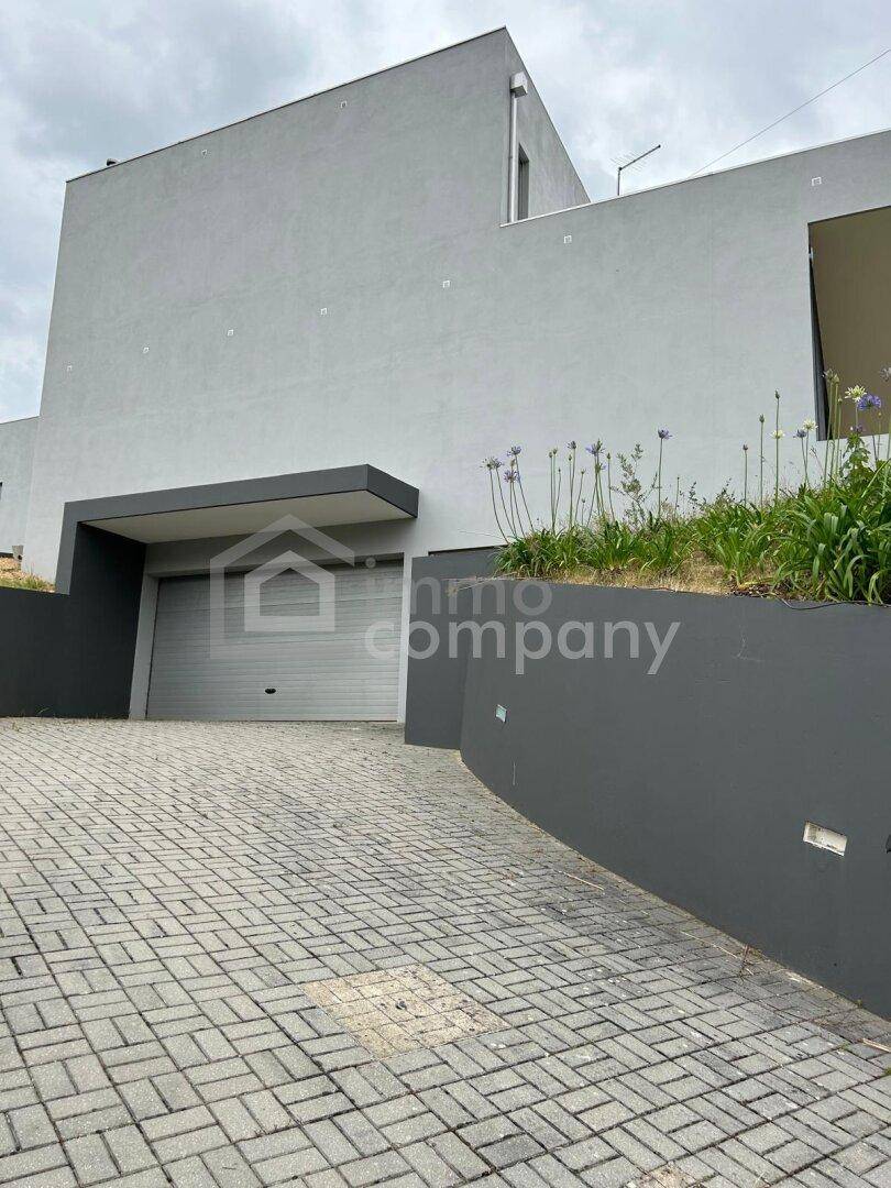 Zufahrt zur Garage der modernen Villa mit gepflastertem Weg und dunklen Mauern.