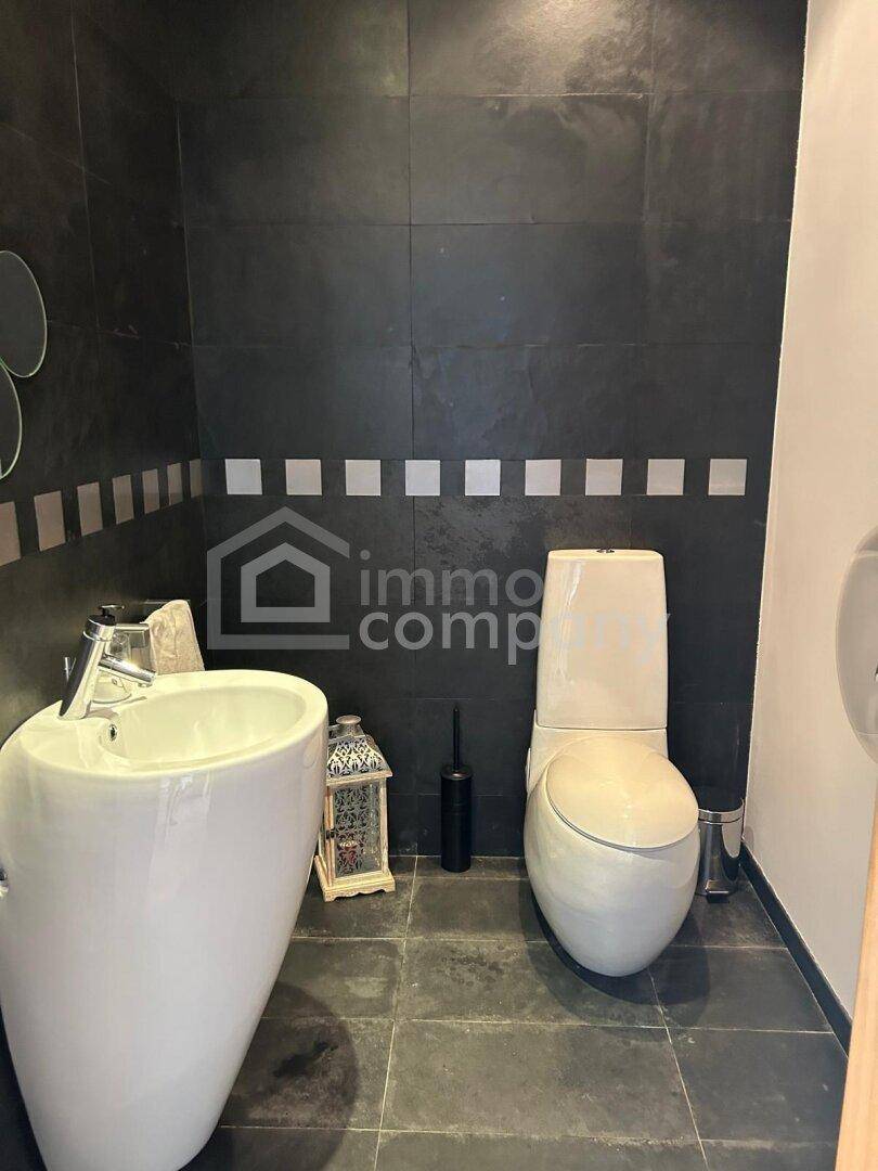 Modernes Gäste-WC mit dunklen Fliesen, weißem Standwaschbecken und Toilette.