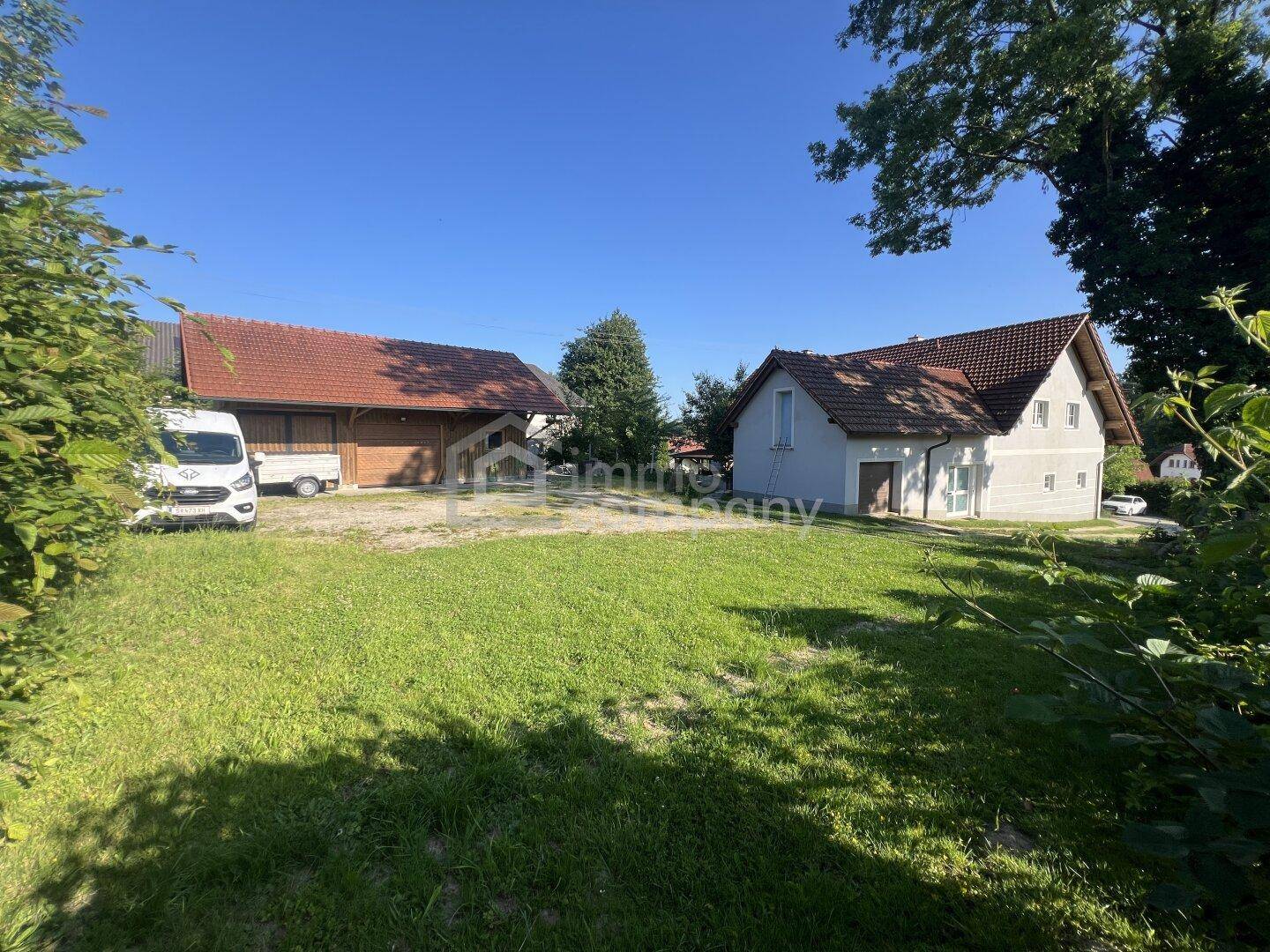 Weitläufiger Gartenbereich mit Rasenfläche und Nebengebäude unter strahlend blauem Himmel.