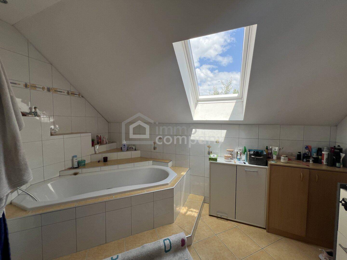 Badezimmer mit Badewanne, Dachschräge und einem Oberlicht für natürliches Licht.