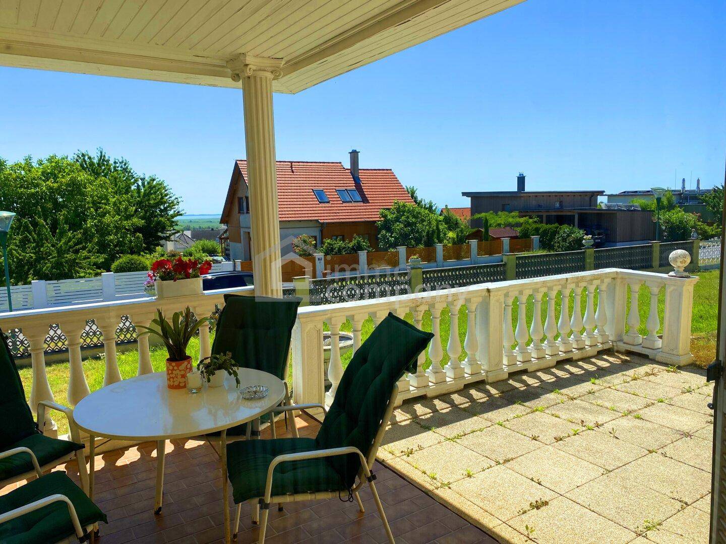 Überdachte Terrasse mit Gartenmöbeln und Blick auf die Nachbarschaft und den See.