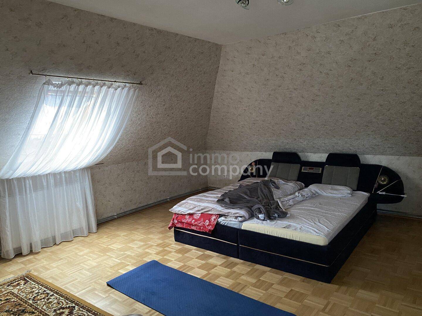 Schlafzimmer im Dachgeschoss mit Doppelbett, schrägen Wänden und Parkettboden.